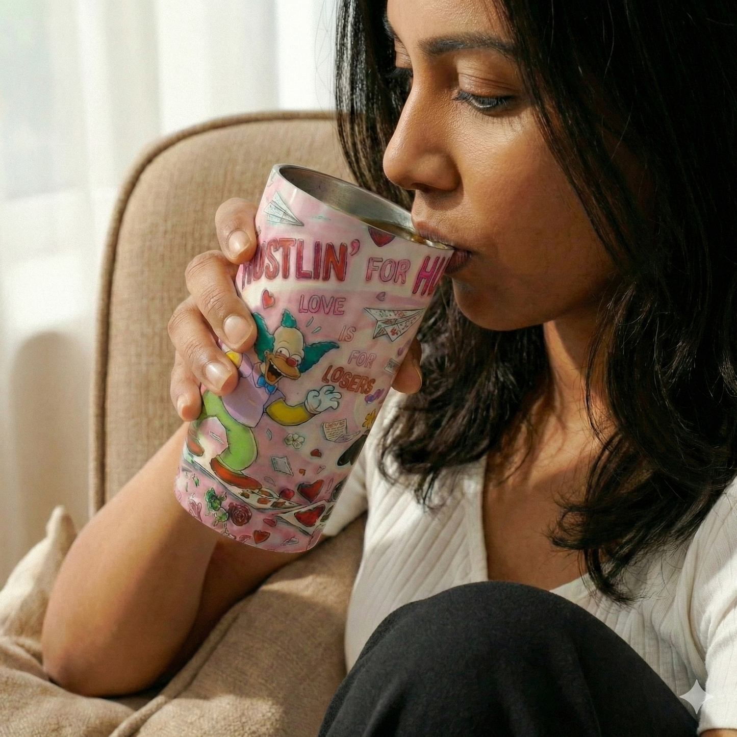 Woman drinking from a colorful mug with cartoon characters in a cozy setting.