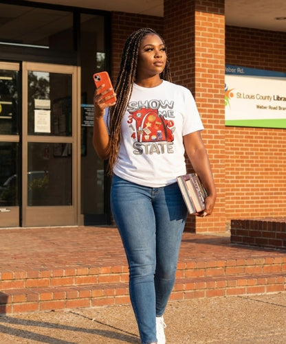Person wearing a white t-shirt with text and graphics, standing outside a building.